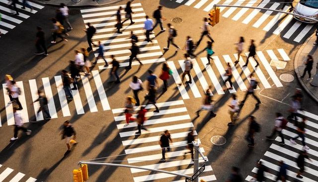 Sunlit pedestrians crossing busy city intersection casting long shadows during golden hour