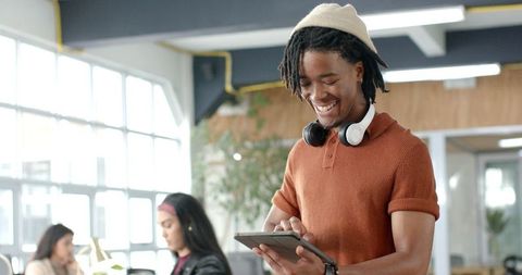 Young professional smiling and tapping tablet in bright coworking space with headphones