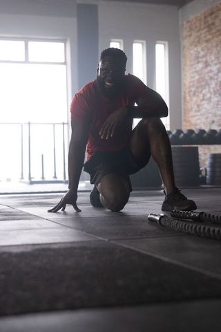 African American Athlete Kneeling, Smiling After Intense Battle Rope Workout in Urban Gym
