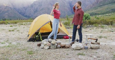 Couple Greeting at Mountain Campsite with Yellow Tent and Camping Gear