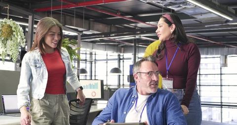 Multicultural team collaborating around workstation in modern sunlit open-plan office