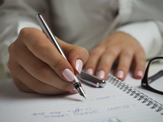 Woman in White Long Sleeved Shirt Holding a Pen Writing on a Paper - Download Free Stock Photos Pikwizard.com