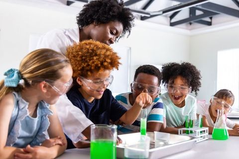 Teacher guiding kids conducting hands-on chemistry experiment wearing safety goggles