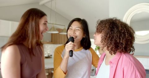 Diverse friends singing karaoke in contemporary kitchen