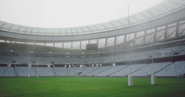 Empty rugby stadium features thick fog covering the field. Seen are empty stands and goalposts with grass on the field. Great for illustrating themes of sports, loneliness, outdoor venues, and seasonal changes. Useful for website banners, articles on sports challenges, and promotional material for sports events.