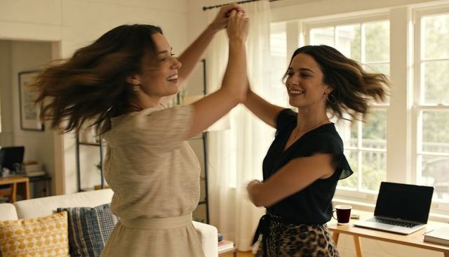 Two women twirling in sunlit living room embracing joyful connection