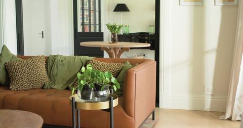Caramel leather tufted sofa with olive green throws and modern side table planter in sunlit living r