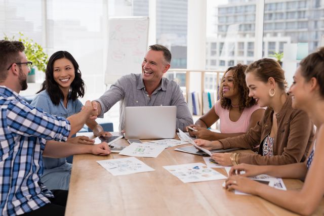 Diverse group of business professionals shaking hands during a meeting in a modern office. Ideal for illustrating concepts of teamwork, collaboration, corporate culture, and successful business partnerships. Suitable for use in business presentations, corporate websites, and marketing materials.