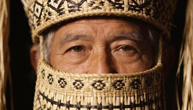Elder man wearing handwoven straw hat and face covering showing intricate woven motifs