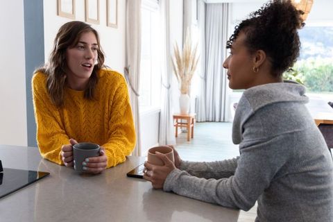 Multiracial friends chatting over coffee at kitchen island wearing cozy sweaters