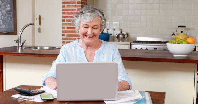 Senior woman using laptop and calculator at home