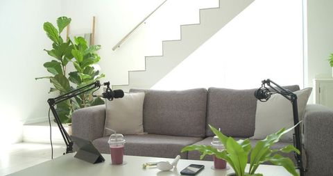 Recording podcast in minimal sunlit home studio with gray sofa and boom microphones