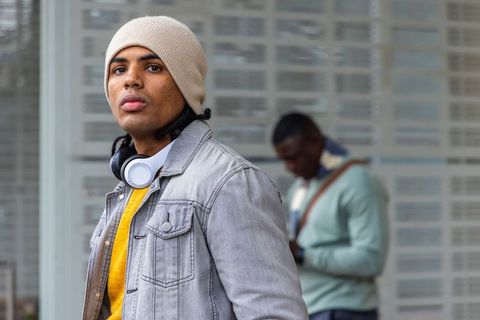 African american commuter waiting at transit stop wearing beanie and headphones, urban street style
