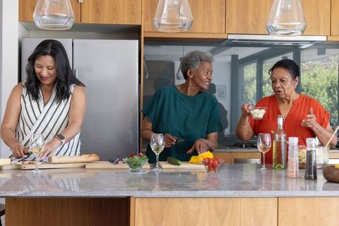 Three african american women preparing meal at kitchen island with wine and fresh produce