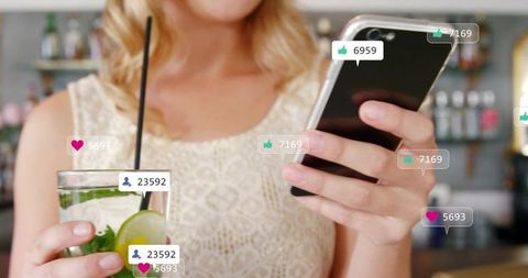 Woman scrolling smartphone at bar holding cocktail with social media likes and followers