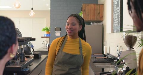 Smiling female barista preparing espresso behind modern cafe counter with grinder and equipment