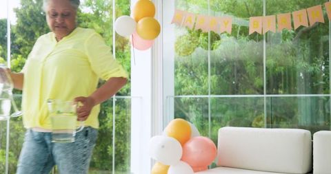 Senior woman cleaning post birthday party with balloons