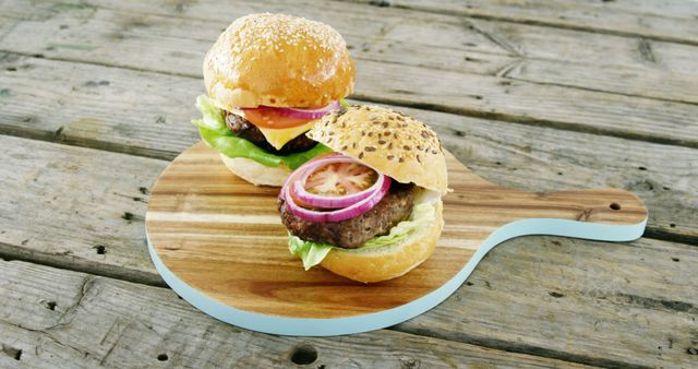 Gourmet beef burgers topped with fresh lettuce, tomato slices, red onion, and cheese served on sesame seed buns. These burgers are presented on a wooden board placed on a well-worn wooden surface. Ideal for use in food blogs, recipe websites, and advertisements focused on quality, homemade meals.