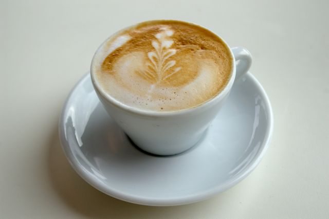 Close-up of beautifully crafted latte art in a white cup on a matching saucer. The frothy design is a leaf or heart shape. Perfect for marketing coffee shops, cafes, barista skills, or articles about coffee culture.