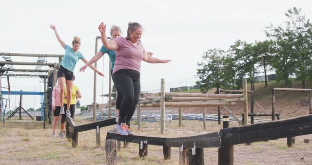 Women balancing on obstacle course beams in park, engaging in outdoor fitness activities. Ideal for content related to health, teamwork, outdoor exercise, community events, and active lifestyles.