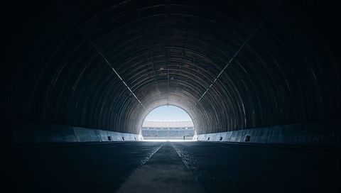 Dramatic ribbed tunnel leading to circular stadium exit with silhouetted figures