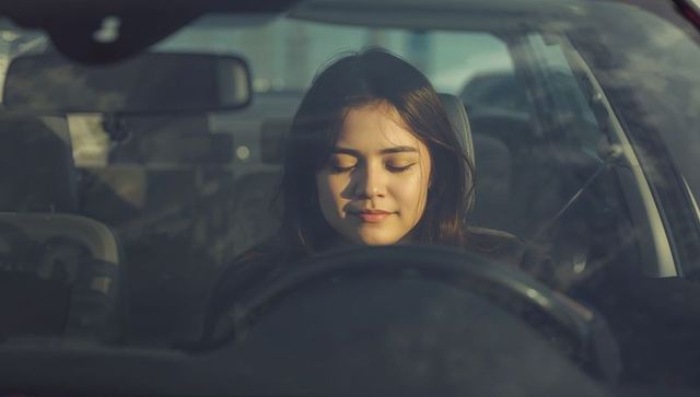 Young woman resting behind wheel in sunlit parked car, calm lifestyle automotive portrait