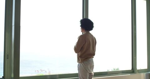 Man Standing and Gazing Through Floor-to-Ceiling Window at Panoramic Ocean View