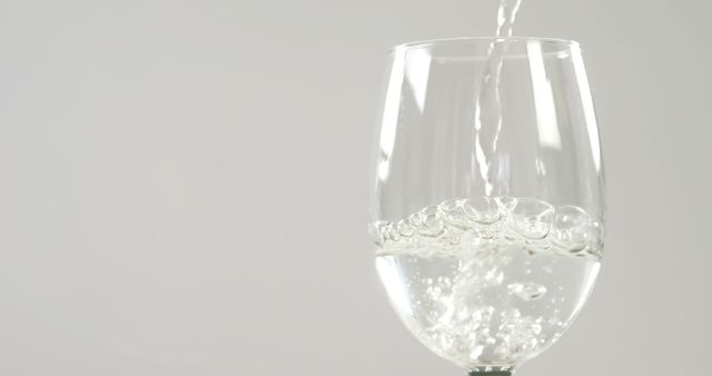 Water is being poured into a clear wine glass against a neutral background, with copy space - Download Free Stock Photos Pikwizard.com