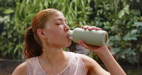 Woman drinking from reusable bottle after workout outdoors hydrating and recovering energy