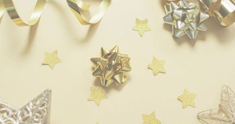 Golden gift bow with glitter star confetti and metallic curling ribbon on cream backdrop