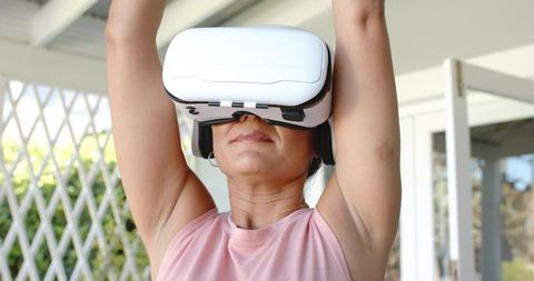 Indian woman wearing vr headset raising arms on sunlit porch enjoying virtual reality