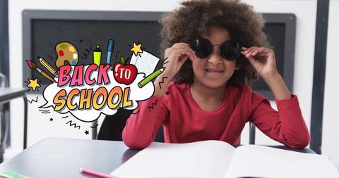 Child wearing sunglasses at school desk with notebook and back-to-school graphic