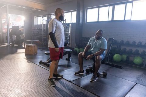 African american workout partners resting and talking by dumbbells in bright gym