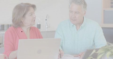 Senior couple reviewing finances at home office kitchen table with laptops and documents