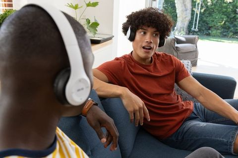Diverse Friends Using Wireless Headphones on Couch in Living Space