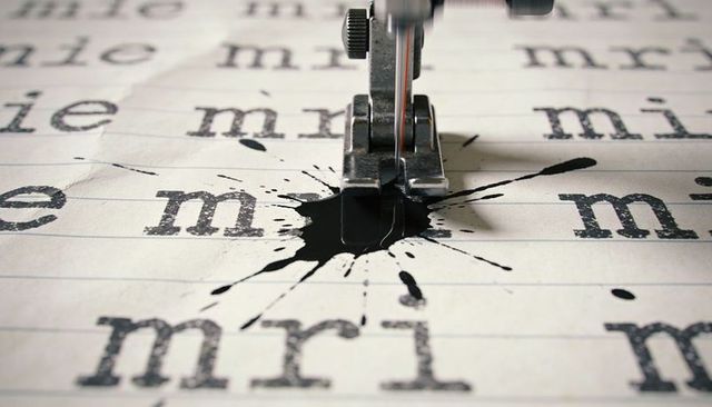 Sewing machine stitching through ink blot on ruled paper with repeated typewriter letters
