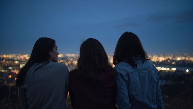 Three friends watching city lights at twilight on hillside
