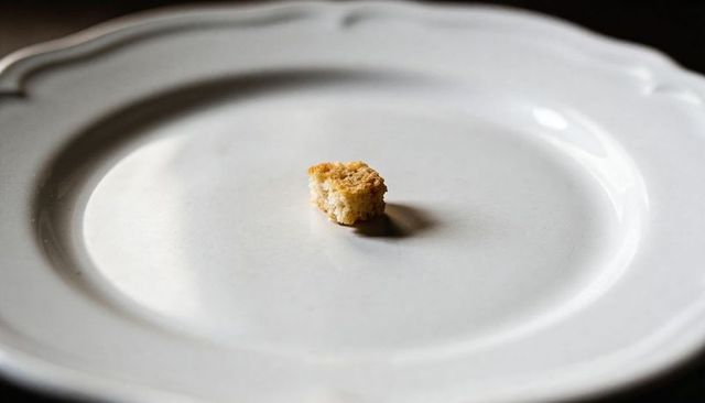Single golden breadcrumb sitting on white porcelain plate casting soft shadow minimalist