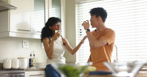 Sunlit modern kitchen couple sipping green drinks and laughing on granite countertop