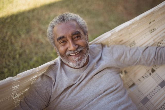 Senior man enjoying a peaceful moment on a hammock outdoors. Ideal for use in advertisements, articles, and promotions related to retirement, leisure activities, senior lifestyle, and outdoor relaxation.