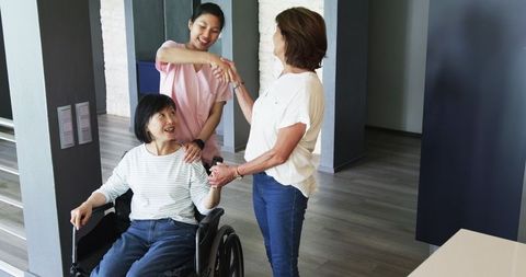 Senior Woman in Wheelchair with Nurse and Friend in Cheerful Hall Meeting