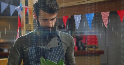 Bearded market vendor examining fresh leafy greens at rustic stall with colorful bunting