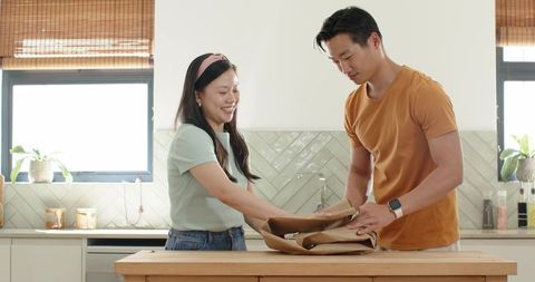 Asian couple unwrapping delivery at sunlit kitchen island, casual home lifestyle moment