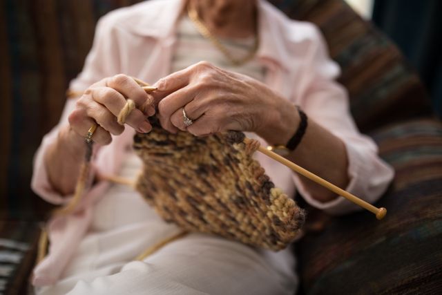 Midsection of senior woman knitting wool while sitting on sofa at retirement home