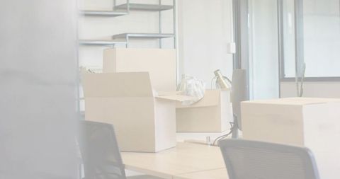 Office desks being packed for relocation with cardboard boxes, desk lamp and shelving