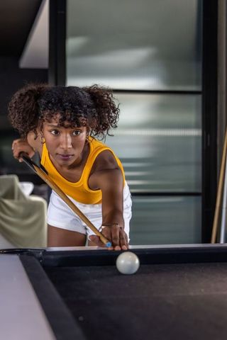 Young woman leaning over pool table lining up focused shot in modern home interior