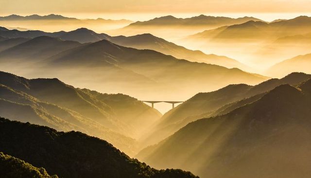 Golden sunrise casting mist over layered mountain ridges with arched concrete viaduct