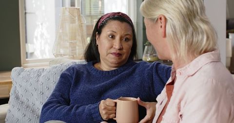 Diverse female friends in warm living room chatting over coffee