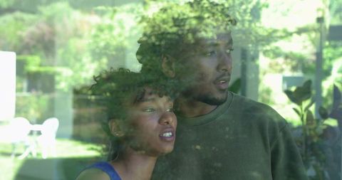 African american couple leaning by window, gazing into garden with soft reflections