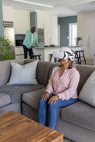Couple relaxing at home while woman experiencing virtual reality headset and partner on laptop